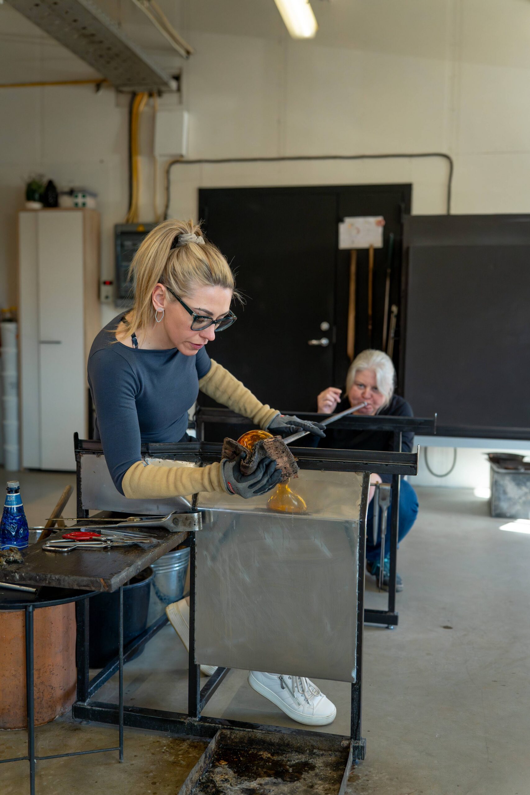 Working with an assistant — the blower shapes the glass object with wet newspaper while the assistant blows the object larger.